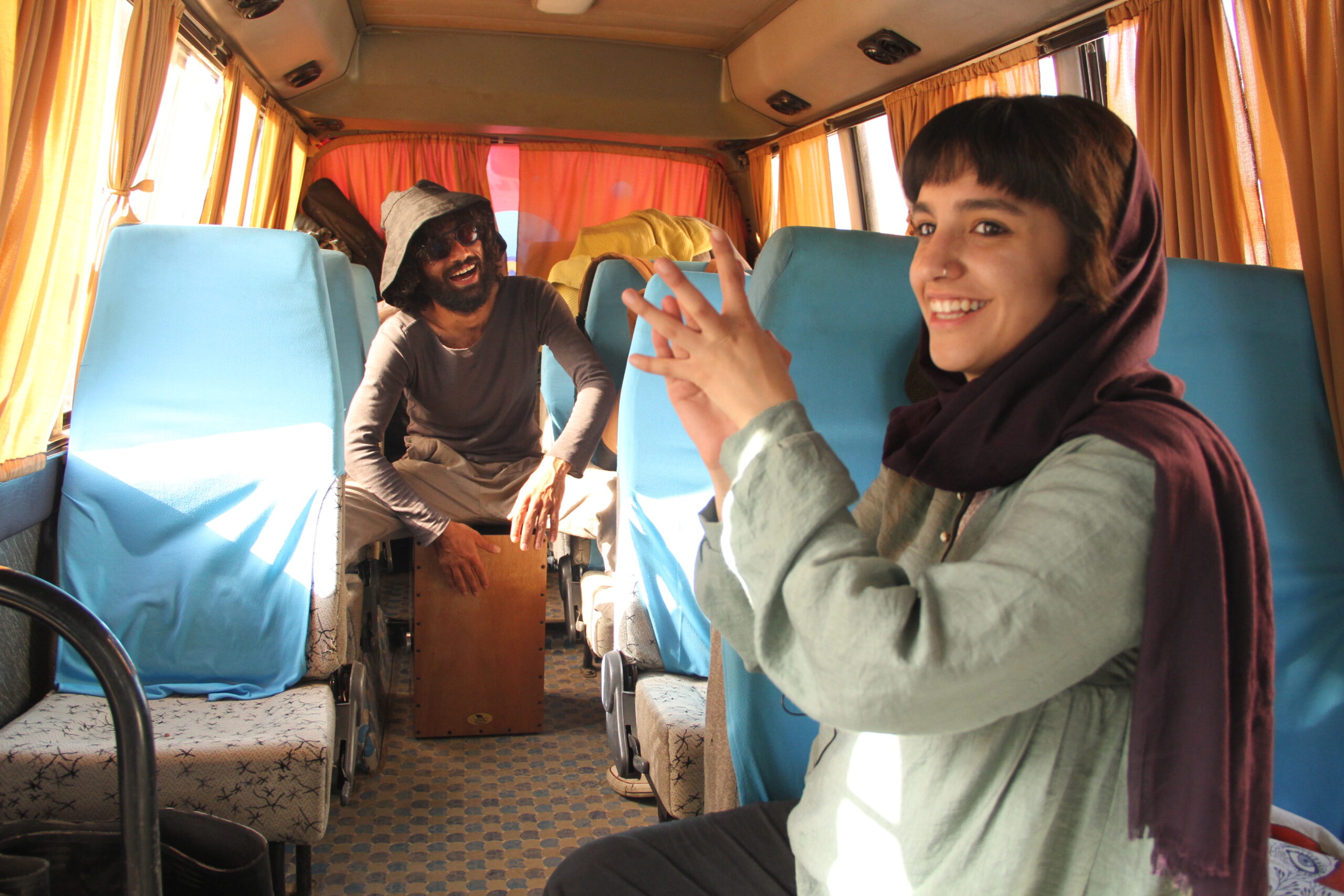 In einem Tourbus, vorne eine junge klatschende Frau, in der Mitte im Hintergrund ein junger männlicher Musiker
